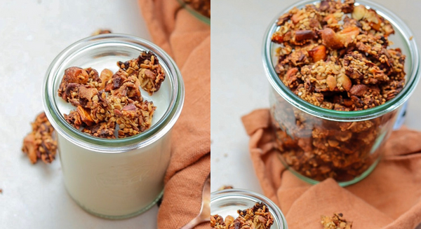 Ein Glas mit Joghurt und zuckerfreiem Granola steht neben einem größeren Vorratsglas und einem Löffel auf einem Tuch.