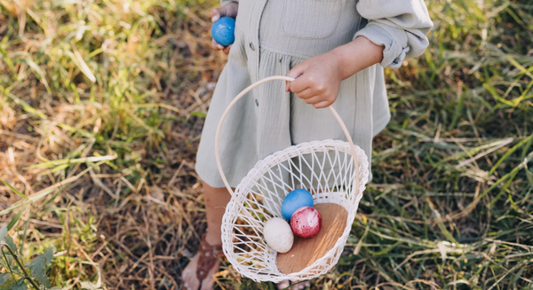 Ein Kind sammelt bunte Ostereier in einem weißen Korb auf einer Wiese.