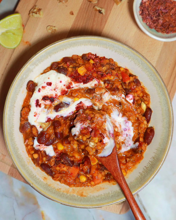 Veganes Chili sin Carne mit roten Linsen, Bohnen und Gemüse, serviert mit Joghurt-Topping in einer Schale auf Holzuntergrund