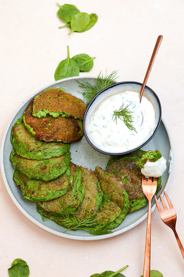 Teller mit goldbraun gebratenen Spinatküchlein, angerichtet mit einem Schälchen frischem Kräuterquark, garniert mit Dill und frischem Spinat