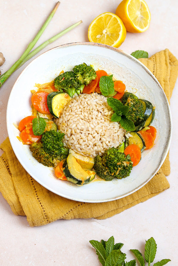 Veganes Gemüse-Curry mit Brokkoli, Zucchini und Möhren, serviert mit Vollkornreis und frischer Minze auf einem weißen Teller.